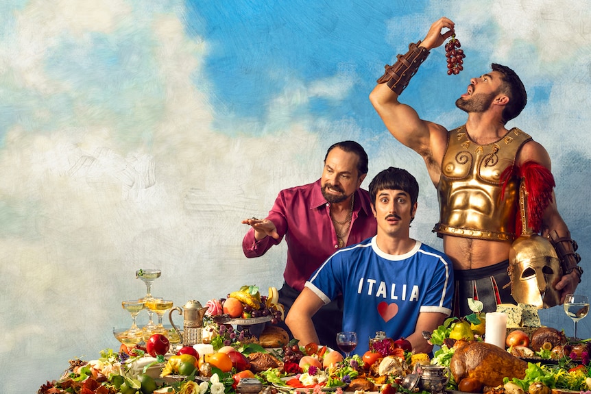 An older Italian man leans over the shoulder of a shocked looking young Italian man, as a gladiator eats grapes behind them.