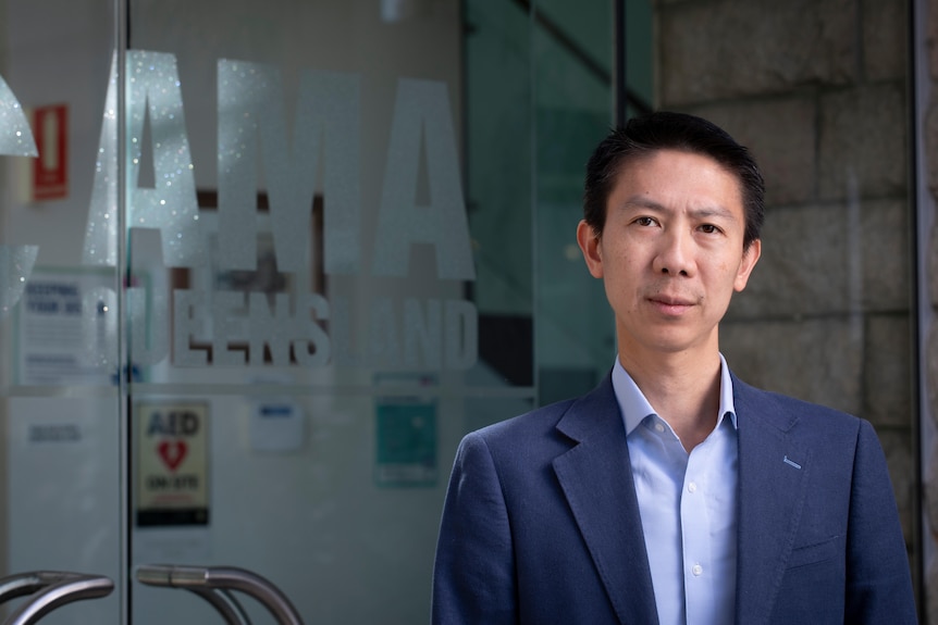 A man (Nick Yim) standing near an AMA Queensland logoed door with a serious expression.