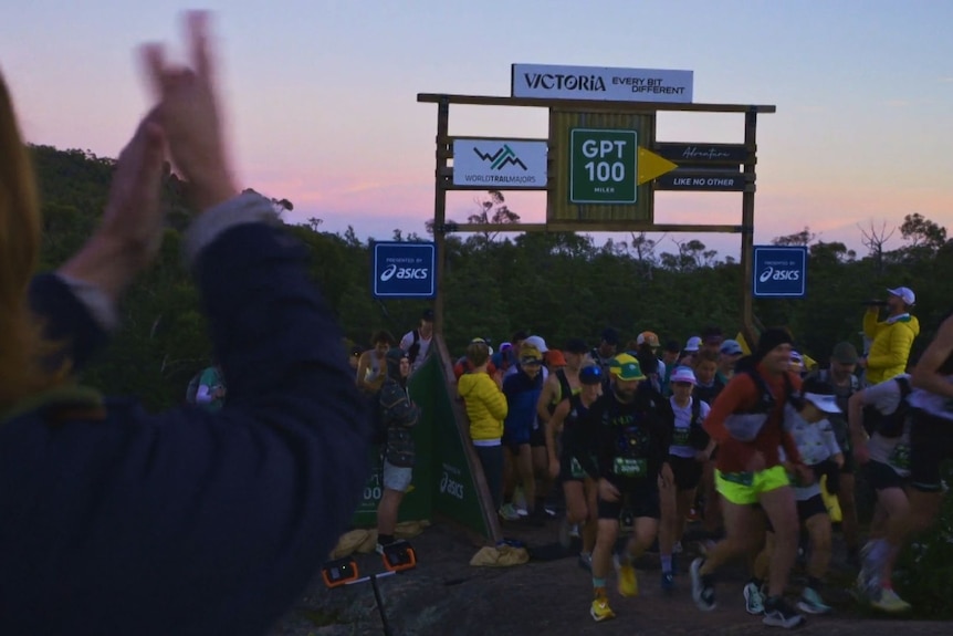 A large group of runners begin their race on rocky terrain in the early morning.