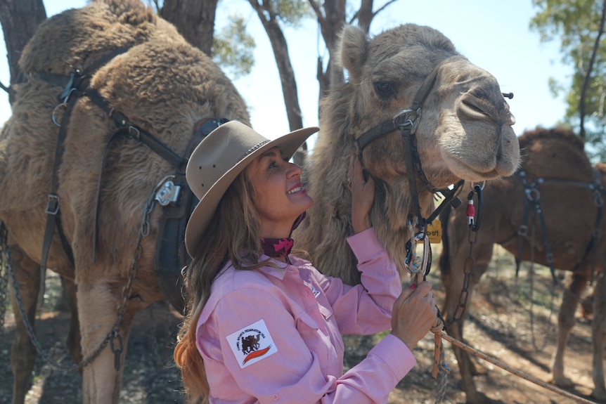 A woman in pink short and cowboy hat talks to a camel