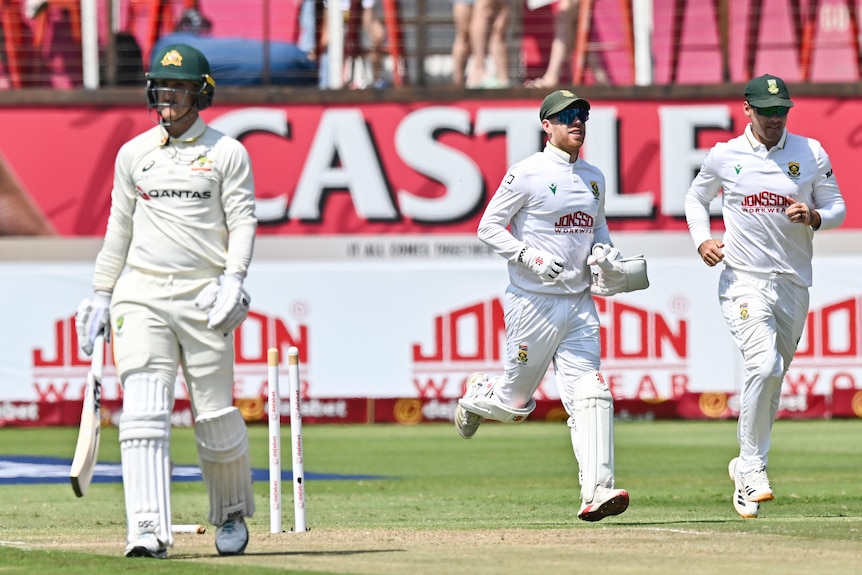 A cricket batter in white walks off the field with players behind him