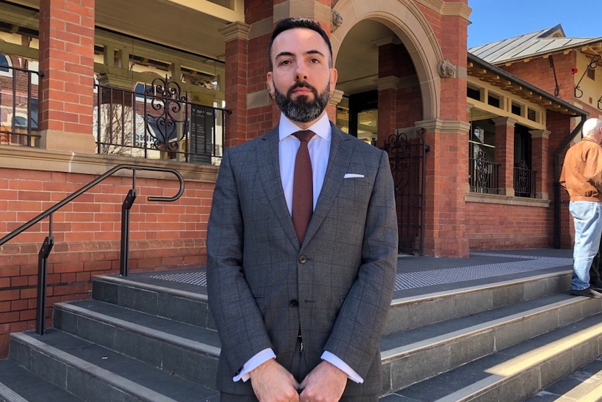 A man in a suit stands on the steps of a red brick court house
