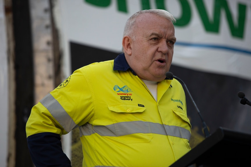 A man wearing a construction outfit, speaking at a lectern.