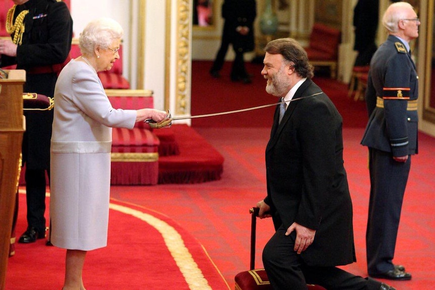 Bryn Terfel kneels during an investiture ceremony. The queen touches his shoulder with a ceremonial sword.