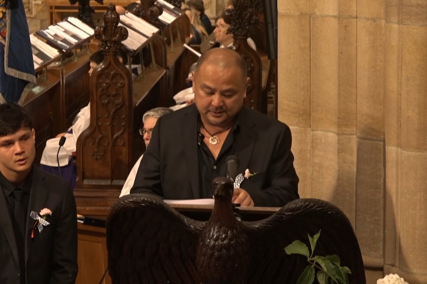 Man dressed in black speaks in church, behind bird-shaped lecturn