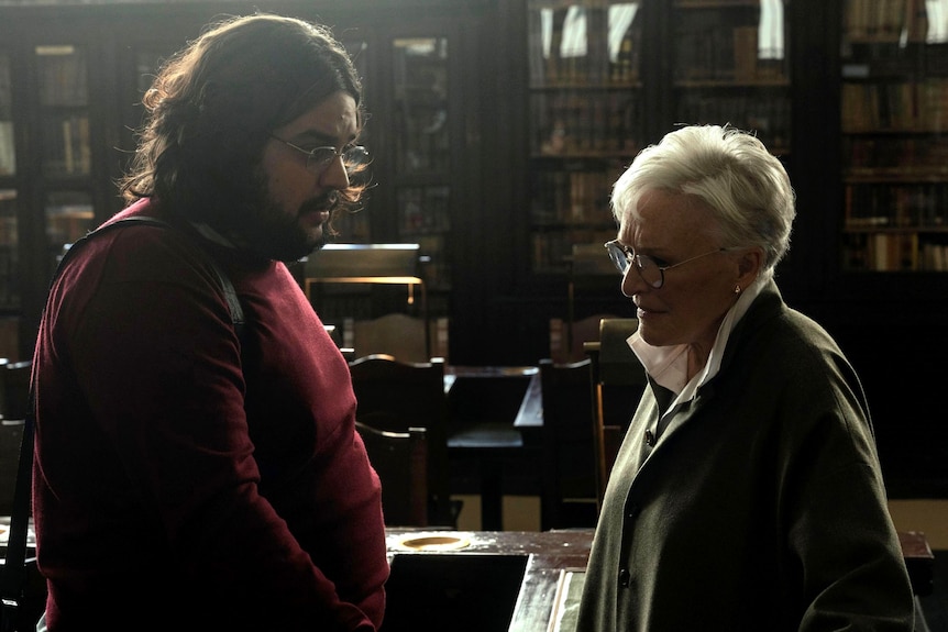 A man and a woman stand opposite each other in a library.