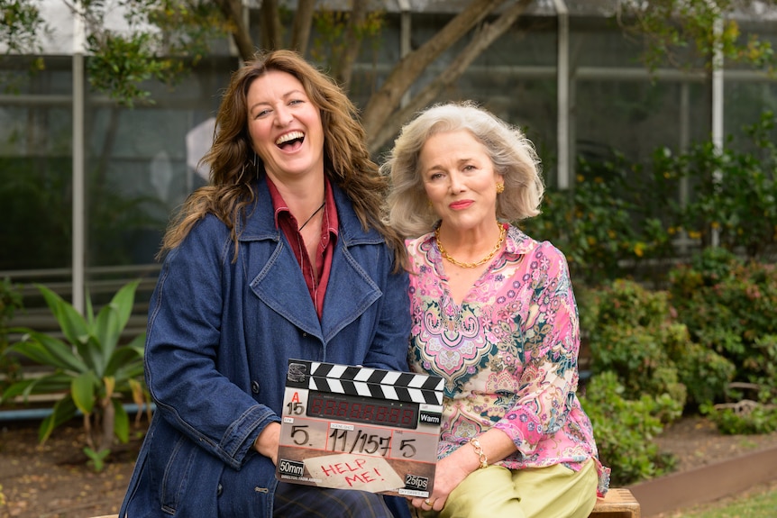 Kate beams as she holds a clapper next to Sarah, who smiles softly.