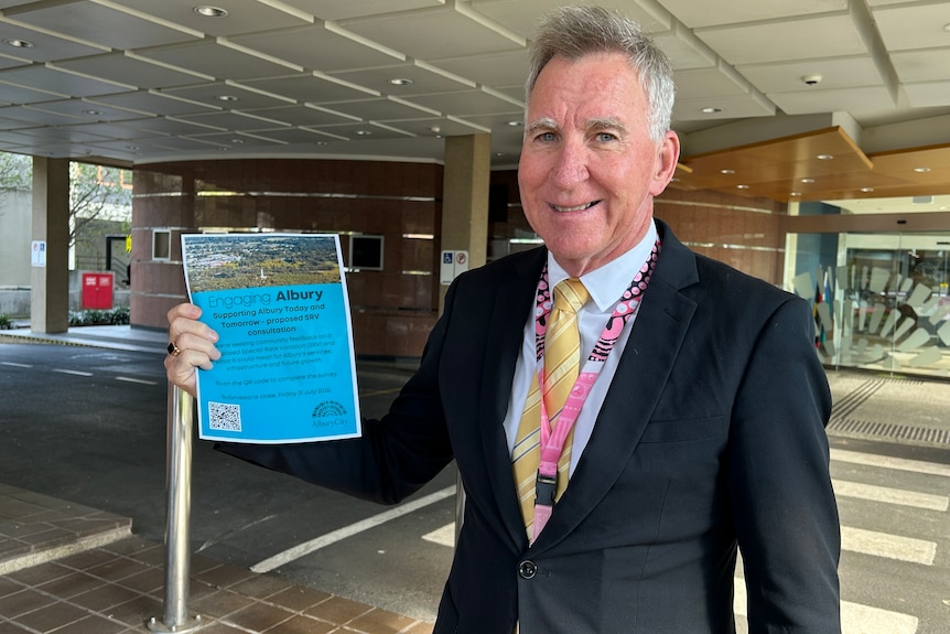 A man in a suit holding a flyer