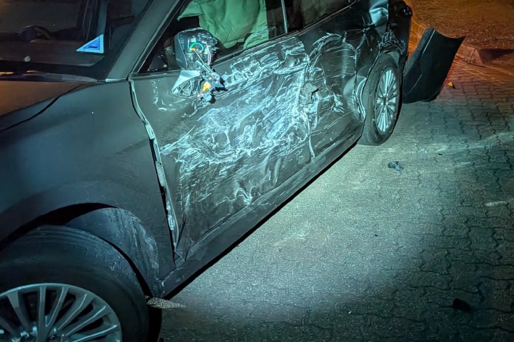 The side of a dark car is completely scraped up and dented, with the wing mirror hanging off.