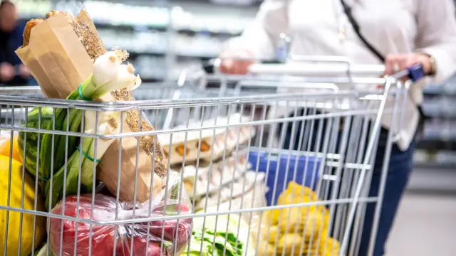 A woman pushes a shopping trolley down a supermarket aisle.