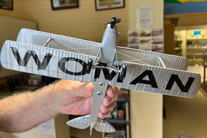 A model plane with WOMAN written in large bold text on the bottom of the wings.