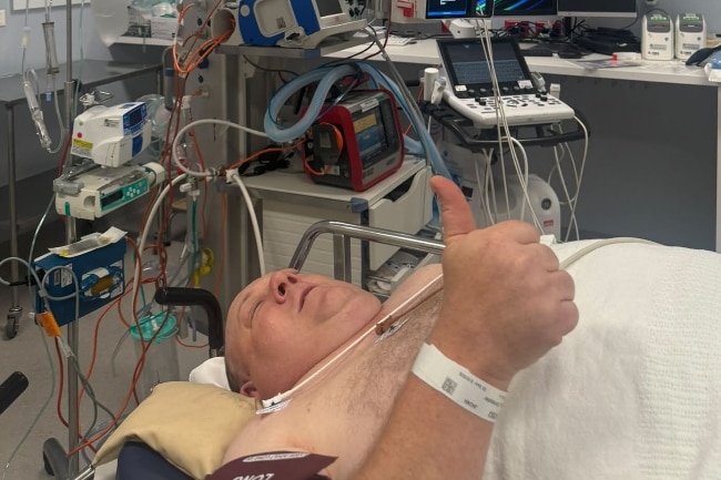 A man lying in a hospital bed giving a thumbs up.