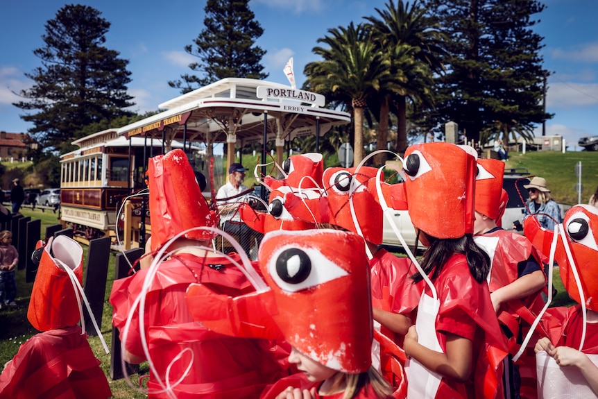 A group of children in handmade krill costumes standing in front of a heritage tram with a sign that says 'Portland'.