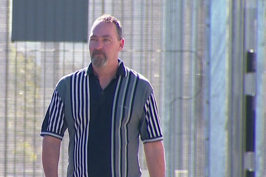 A man in a stripe polo top walks past a prison fence