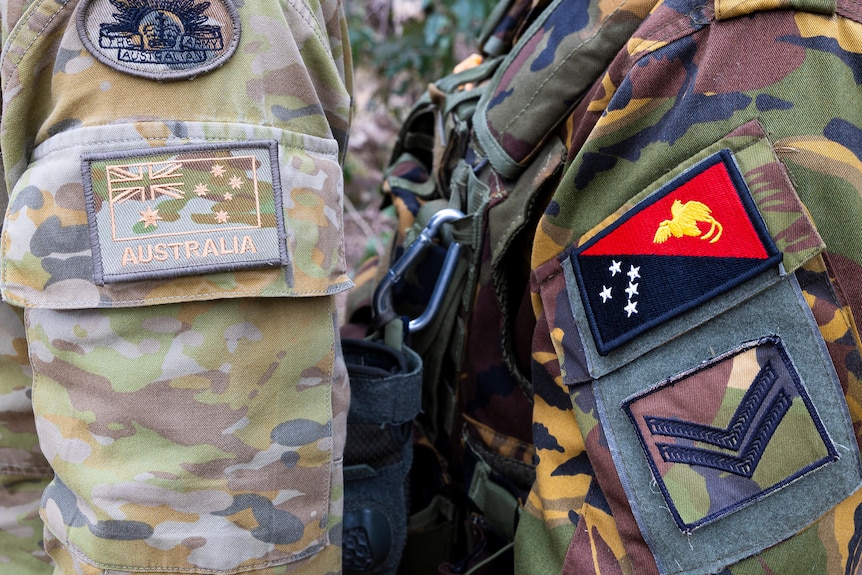 The insignia on the arms of two uniformed soldiers, one showing the Australian flag, and the other the PNG flag.