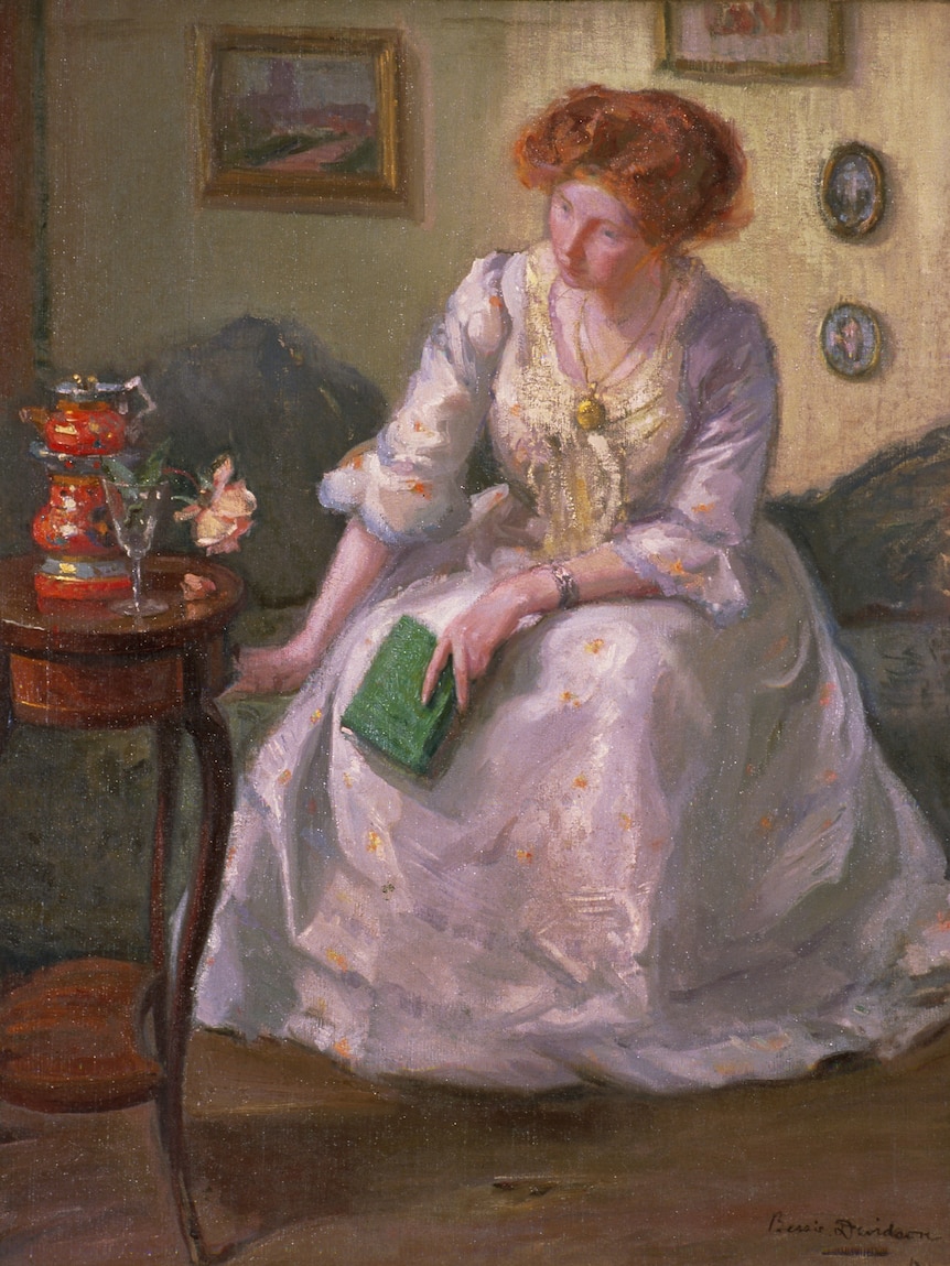 Oil painting of a young woman with red hair in a long dress on a chaise, looking down, holding a green book
