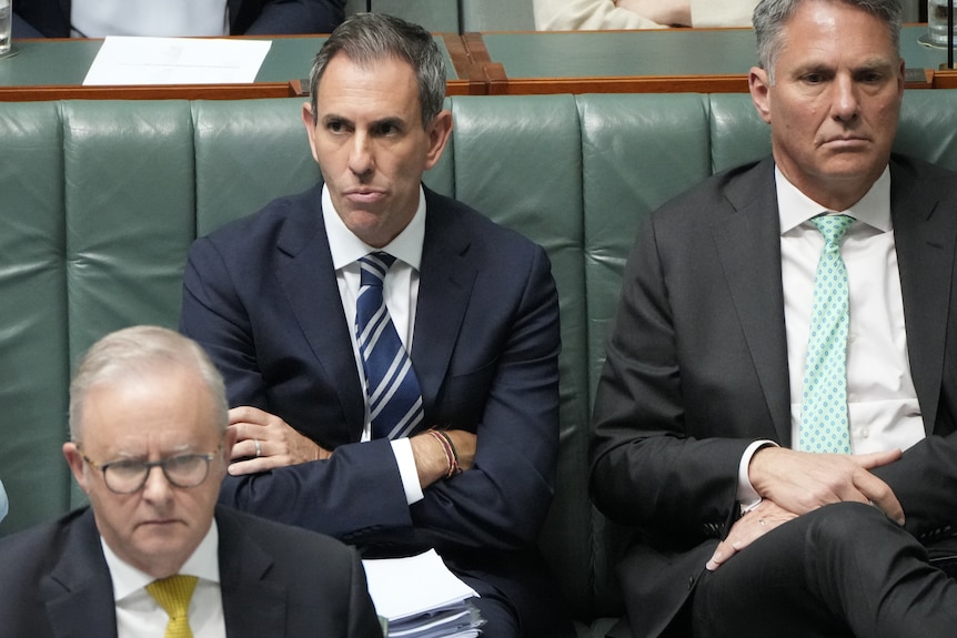 Jim Chalmers sits with crossed arms in parliament, Anthony Albanese in front of him.