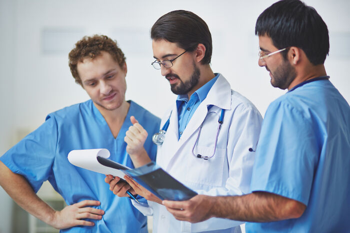 Three doctors and nurses in scrubs discussing patient medical charts together.