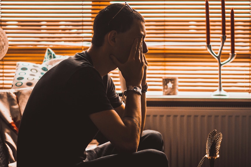 A man holds his head in his hand and looks serious.
