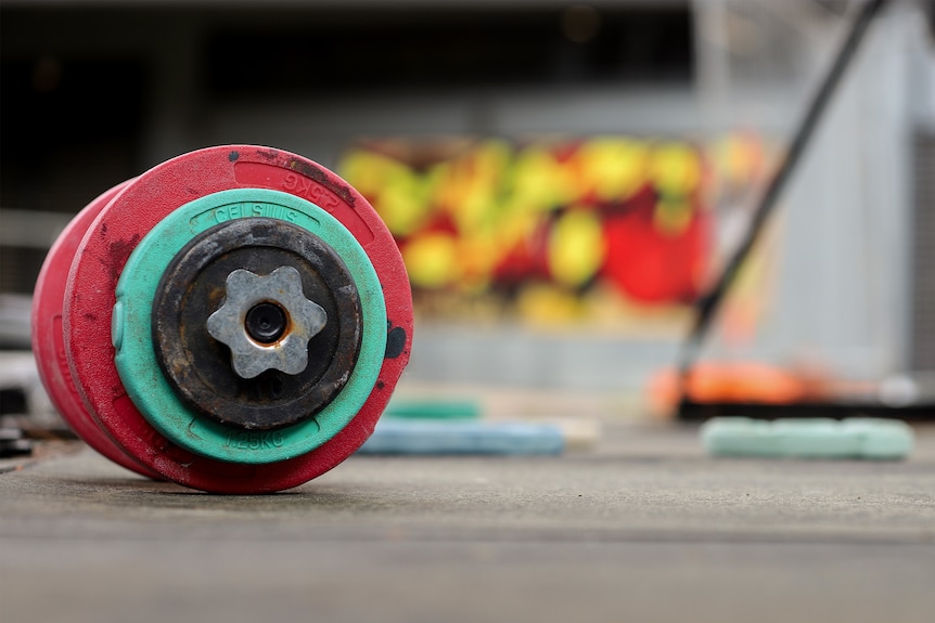 A set of weights lie on the ground with a colourful mural in the background