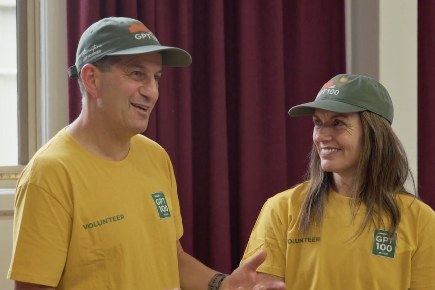 At night, Greg and Nicole Kew cross a finish line with their arms in the air.