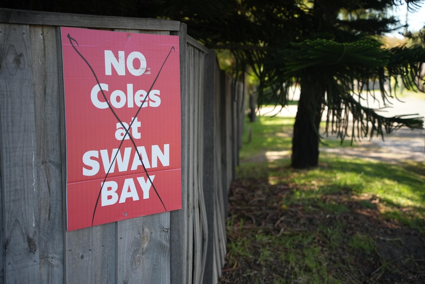 A red sign with white lettering saying "No Coles at Swan Bay" hangs from a suburban fence in Point Lonsdale. 