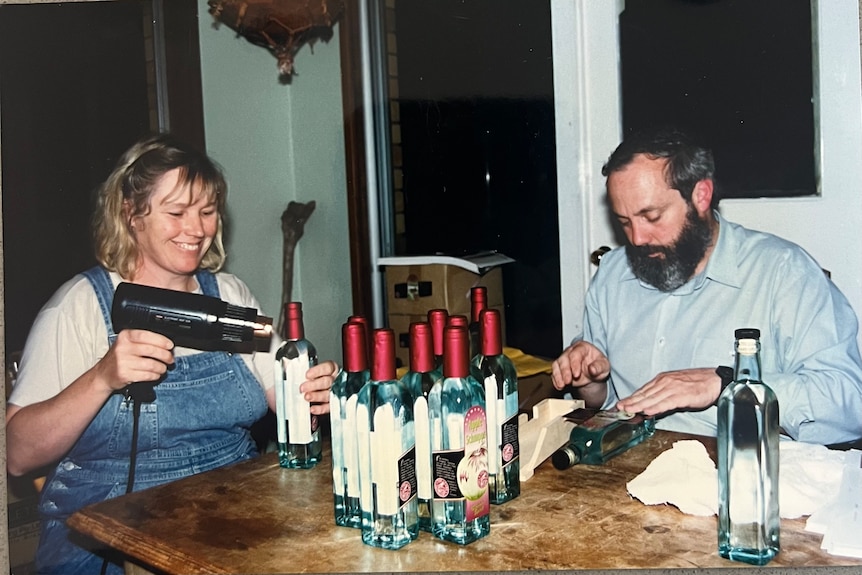 A man and woman apply labels to clear whisky bottles on their dining table in the 1990s.