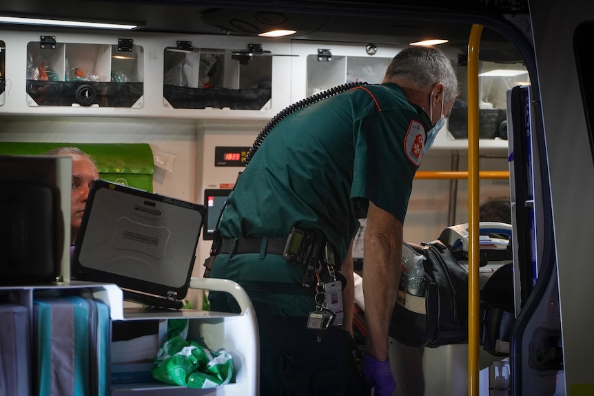 A man in a green uniform bends over inside an ambulance