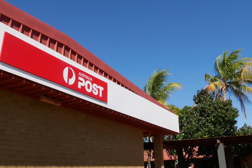 A red Australia Post sign against a blue sky with palm trees in the background.