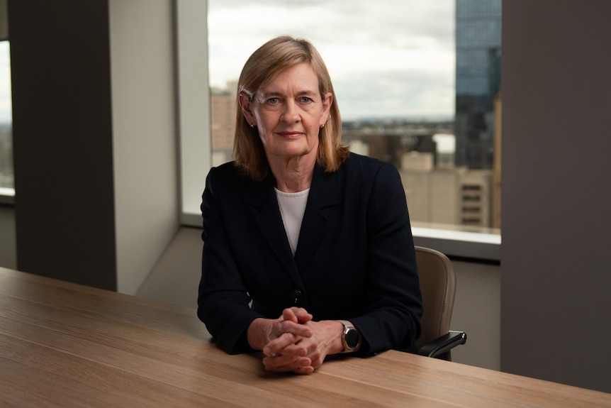 Sarah Court, dressed in a blazer and white shirt, sits at a conference table.