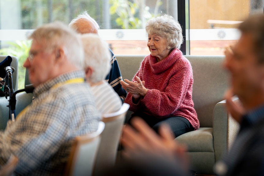 Mature-aged people sit in rows of chairs looking ahead, listening to music.