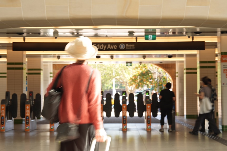A woman wearing a hat and pulling a suitcase make her way to the opal exit gates ale commuter at Central railway station