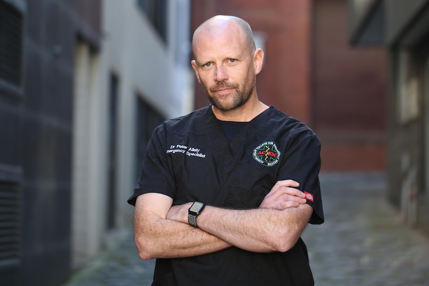 A man in a black scrubs shirt with arms folded looking at camera.