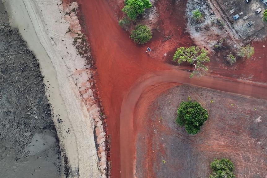 An aerial drone photo of a red dirt road intersection, and trees, a sandy beach and mud flats.