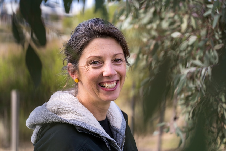 a woman smiles at the camera, she is surrounded by gum trees