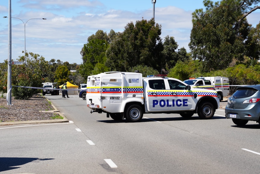 Police officers and vehicles parked on a road with police tape cordoning off a section. 