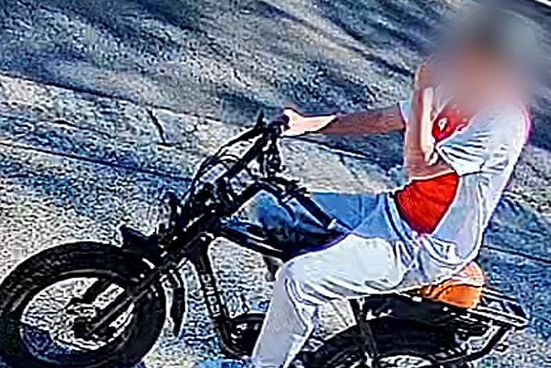a cctv image of a young male wearing a white and organge top riding an e-bike