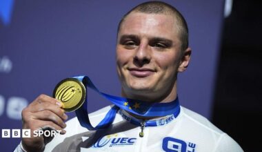 GB cyclist Matt Richardson holds up a gold medal while smiling at the camera