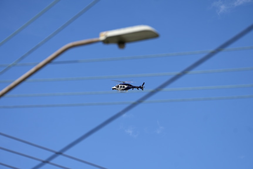 A helicopter seen in the sky in the distance high above a street light.
