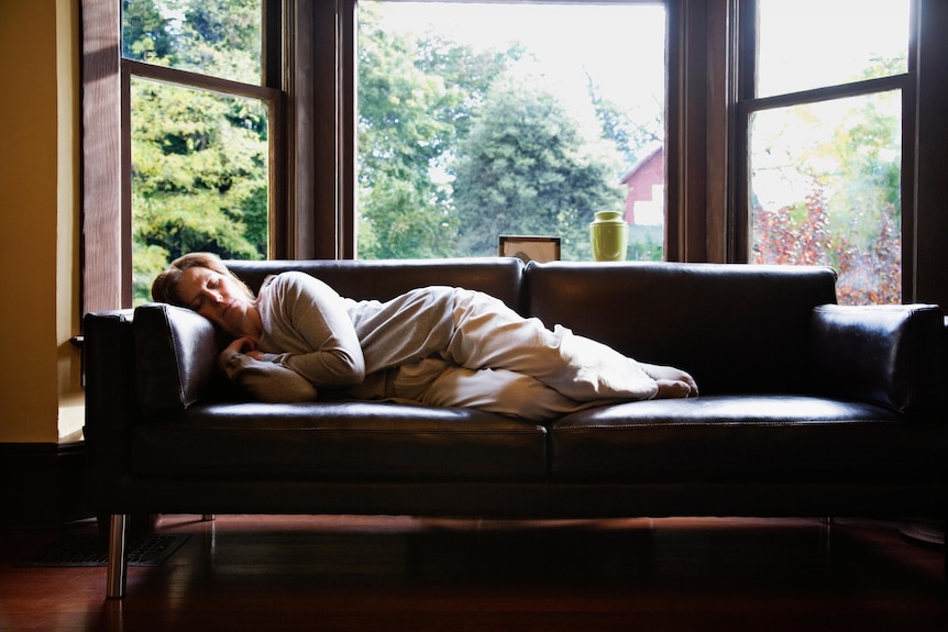 A woman naps on the couch with sunlight pouring in.