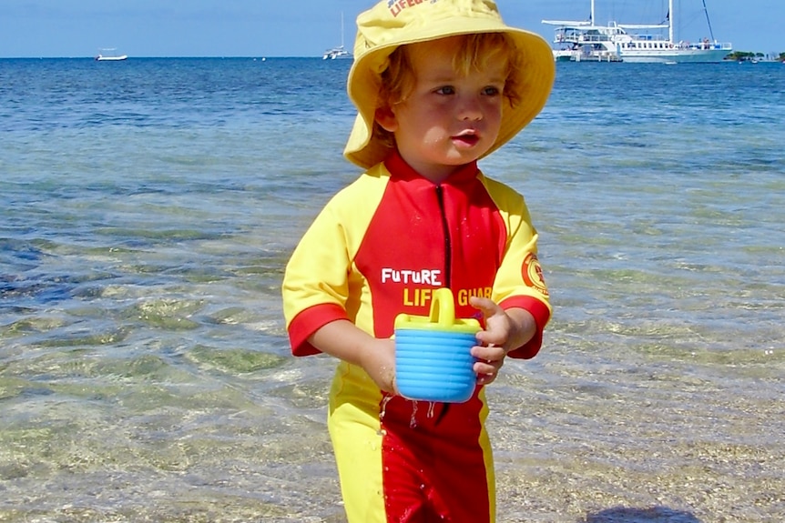 A toddler wearing a lifesaver uniform holding a plastic bucket
