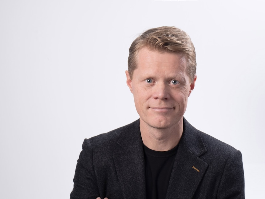 A portrait image of Sam Roggeveen, a white man with blond hair, in a black suit jacket and top with his arms crossed.