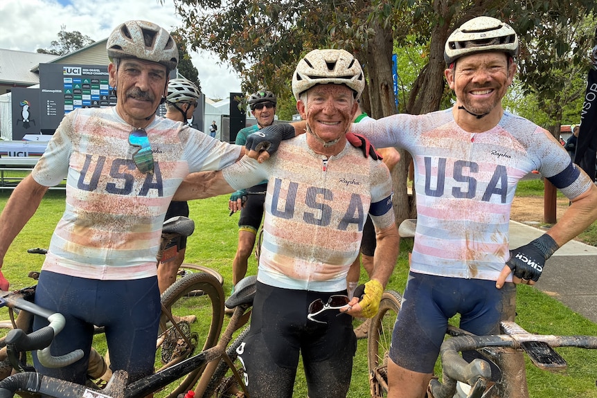 The three men are in a row, smiling and wearing white helmets and USA cycling jerseys.