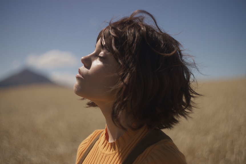 A woman in a field tilts her head towards the sun