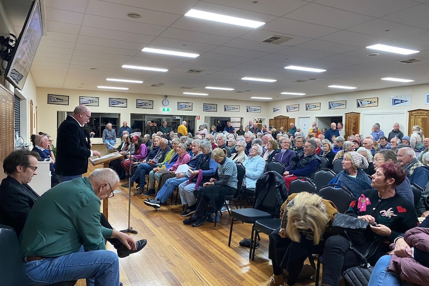 A group of more than 80 people mostly with grey hair sit in the Point Lonsdale bowls club at a community meeting. 