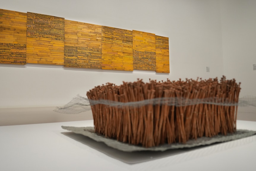 Yellow artwork in focus that looks like a brickwall with writing, the front centre of the image is a cluster of brown nails
