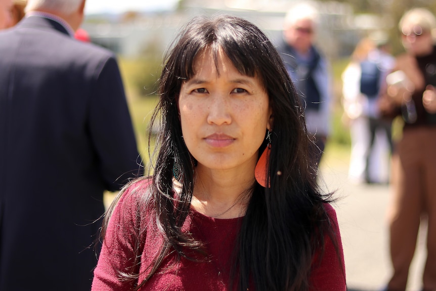 A headshot of Jacqueline, who wears a maroon shirt and large red earings.