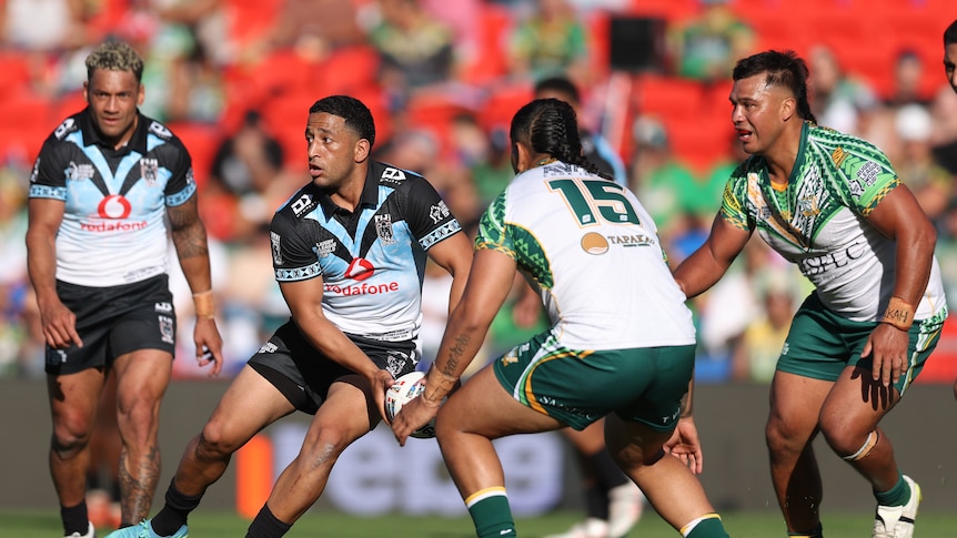 A Fijian rugby league player shapes to pass wide as the Cook Islands defensive line moves up.