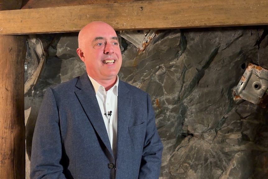 A bald man in a blue jacket smiles to someone off camera