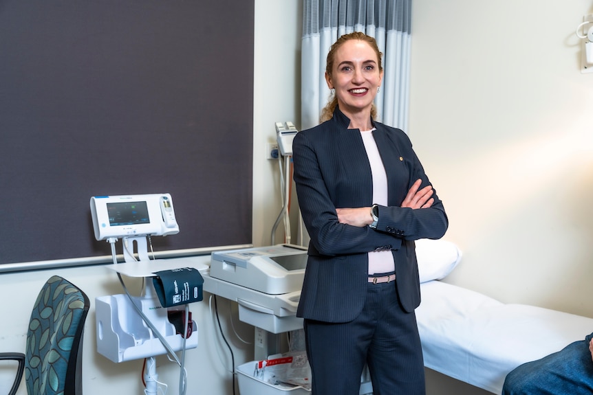Georgina Long crosses her arms in a room with medical equipment.